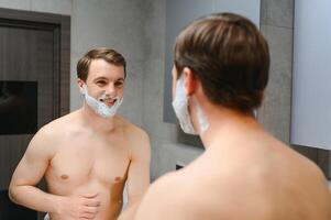 Mature handsome man shaving in front of mirror photo