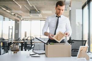 Sad Fired. Let Go Office Worker Packs His Belongings into Cardboard Box and Leaves Office. Workforce Reduction, Downsizing, Reorganization, Restructuring, Outsourcing. Mass Unemployment Market Crisis photo