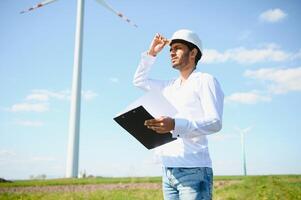 Engineer India man working at windmill farm Generating electricity clean energy. Wind turbine farm generator by alternative green energy. Asian engineer checking control electric power photo