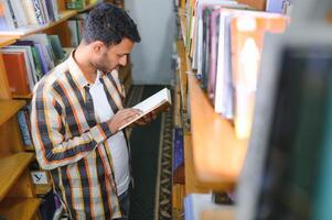 contento inteligente indio o árabe chico, mezclado carrera masculino, Universidad alumno, en el biblioteca foto