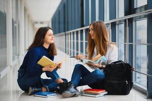 two pretty female students with books sitting on the floor in the university hallway photo