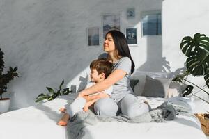 happy woman having fun with adorable son in pajamas in bedroom on mothers day. photo