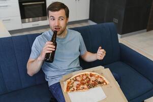 Eats pizza while watching TV show. Man with beard indoors. photo