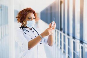 Young smiling African American doctor in medical mask holding a syringe photo