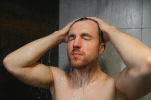 cerca arriba atractivo joven desnudo triste preocupado joven hombre tomando ducha. foto