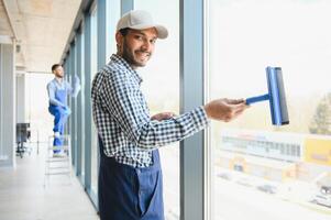 Male janitor cleaning window in office photo