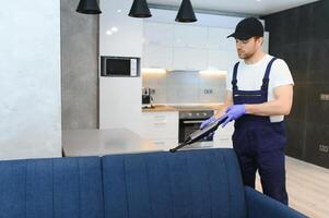 limpieza servicio. hombre portero en guantes y uniforme vacío limpiar sofá con profesional equipo. foto