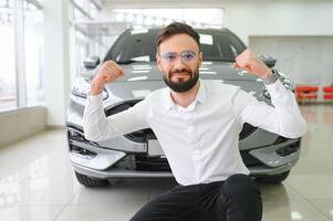 contento joven chico comprobación nuevo lujo auto, comprando automóvil a concesión centro. retrato de alegre milenario caucásico hombre examinando auto a sala de exposición Tienda foto