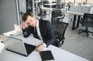 Depressed young businessman holding head in hands, has problem, a laptop on the desk. A guy made a mistake in a work photo