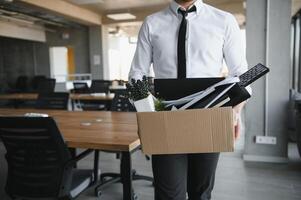 Young handsome businessman in light modern office with carton box. Last day at work. Upset office worker is fired. photo