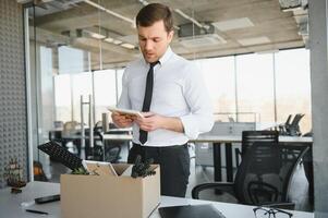 Sad Fired. Let Go Office Worker Packs His Belongings into Cardboard Box and Leaves Office. Workforce Reduction, Downsizing, Reorganization, Restructuring, Outsourcing. Mass Unemployment Market Crisis photo