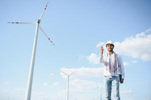 Engineer India man working at windmill farm Generating electricity clean energy. Wind turbine farm generator by alternative green energy. Asian engineer checking control electric power photo