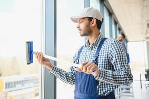 Indian Male professional cleaning service worker cleans the windows and shop windows of a store with special equipment photo