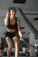 Athletic Female in a Gym Exercises with Battle Ropes During Her Fitness Workout High-Intensity Interval Training. She's Muscular and Sweaty photo