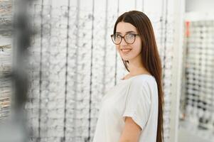 eyesight and vision concept - young woman choosing glasses at optics store. photo