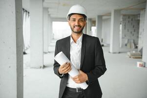 Indian construction site manager standing wearing helmet, thinking at construction site. Portrait of mixed race manual worker or architect. photo