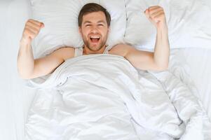 alegre hombre despertar arriba acostado en acogedor cama a hogar en fin de semana Mañana. sano dormir concepto foto