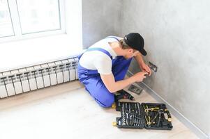 sonriente profesional electricista en uniforme reemplazando un enchufe en Departamento después renovación trabajo foto