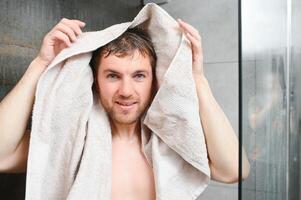 Cheerful young man wiping face with soft towel after washing it in the morning photo