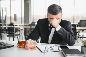 Alcoholism at work. Tired employee drinking alcohol at workplace, can not handle stress photo