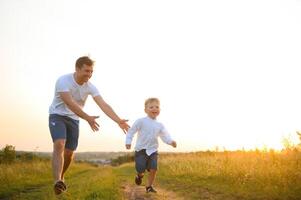 del padre día. contento familia padre y niñito hijo jugando y riendo en naturaleza a puesta de sol foto