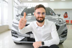 contento joven chico comprobación nuevo lujo auto, comprando automóvil a concesión centro. retrato de alegre milenario caucásico hombre examinando auto a sala de exposición Tienda foto