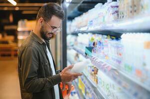 hermoso hombre comprando algunos sano comida y bebida en moderno supermercado o tienda de comestibles almacenar. estilo de vida y consumismo concepto foto