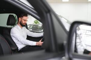 Happy caucasian man in formal wear getting inside luxury modern car for testing interior before purchase. Concept of dealership, selling and purchase photo