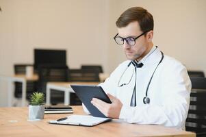 male doctor using tablet computer at his office. General practitioner using digital tablet at his clinic. photo