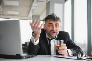 Old male employee drinking alcohol at workplace photo