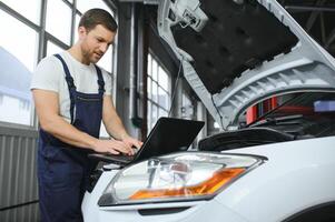 car mechanic using a computer laptop to diagnosing and checking up on car engines parts for fixing and repair photo