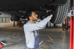 latin hispanic auto mechanic in uniform is examining a car while working in auto service photo