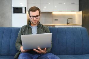 Young cheerful man sitting on sofa with laptop photo