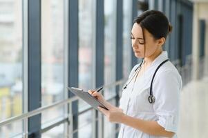 retrato de joven hembra médico en pie en hospital corredor. caucásico mujer trabajando en enfermería hogar. foto