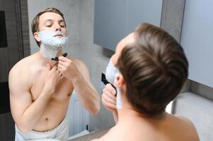 Mature handsome man shaving in front of mirror photo