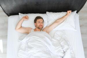 joven hombre dormido despertar arriba y extensión en su cama foto