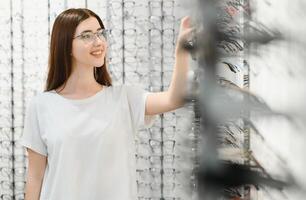 Young Woman with Eyeglasses in Optical Store - Beautiful girl wearing glasses in optician shop photo