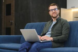 Side view handsome young businessman in eyewear working with computer. Pleasant happy man communicating in social network, searching information online photo