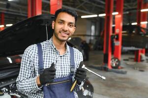 latín Hispano auto mecánico en uniforme es examinando un coche mientras trabajando en auto Servicio foto