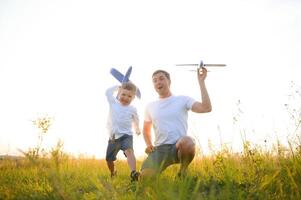 contento padre niño momento. padre llevar a cuestas su chico a puesta de sol mientras él es jugando con juguete avión. foto