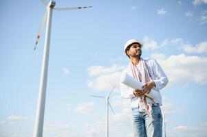 Engineer India man working at windmill farm Generating electricity clean energy. Wind turbine farm generator by alternative green energy. Asian engineer checking control electric power photo