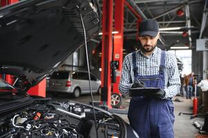 profesional caucásico coche mecánico con Lista de Verificación en pie por vehículo motor zona con capucha abierto detector mal funcionamiento foto