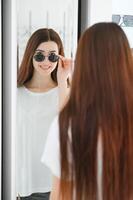 joven mujer elige Gafas de sol para sí misma en un óptica Tienda foto