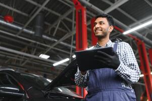 latin hispanic auto mechanic in uniform is examining a car while working in auto service photo