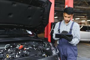 hombre coche técnico mecánico reparando coche problema de motor, durante sistema comprobación detalle, utilizando tableta computadora para mantenimiento y fijación en coche cochera. foto