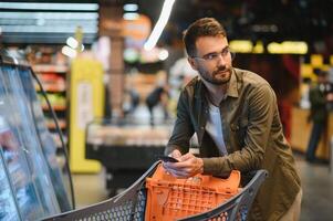 Handsome man hold shopping cart. Man holds shopping trolley. Store, shopping, sales and discounts. Male shopper. Man with shopping trolley at store. photo