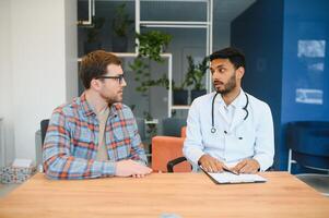 medicine, healthcare and people concept - indian doctor young male patient meeting at hospital photo