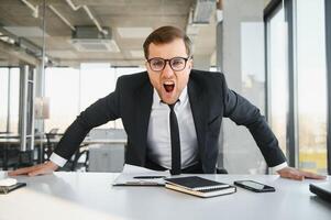 Angry businessman sitting at his desk and screaming at his employees. photo