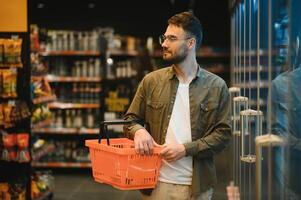 Portrait of smiling handsome man grocery shopping in supermarket, choosing food products from shelf photo