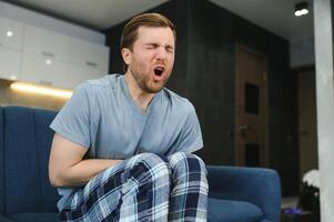 Guy with a beard feeling unwell with a stomach ache while sitting in a couch at home photo